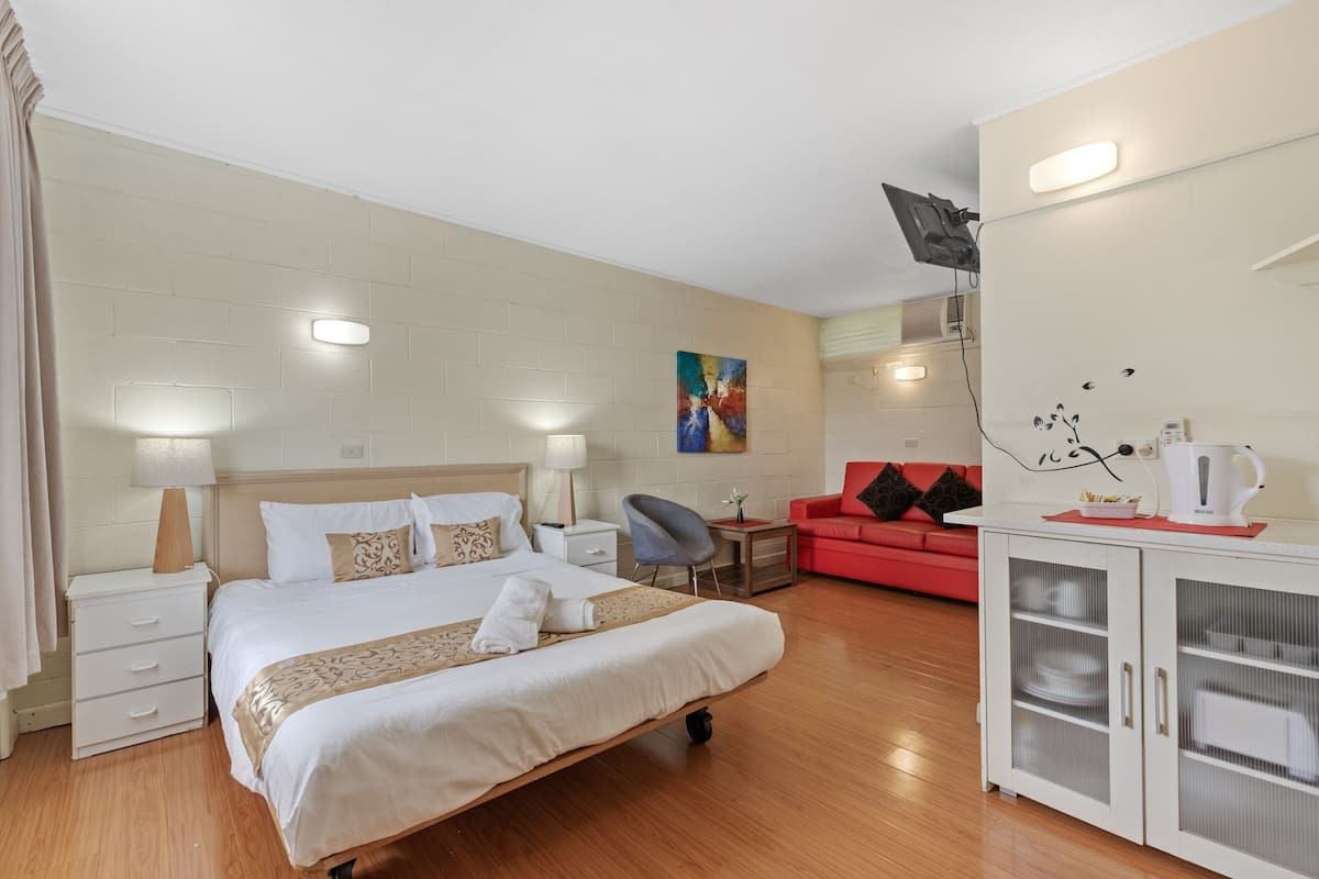 A hotel room with a bed, bedside tables, a desk, a red sofa, and a cabinet with glass doors.
