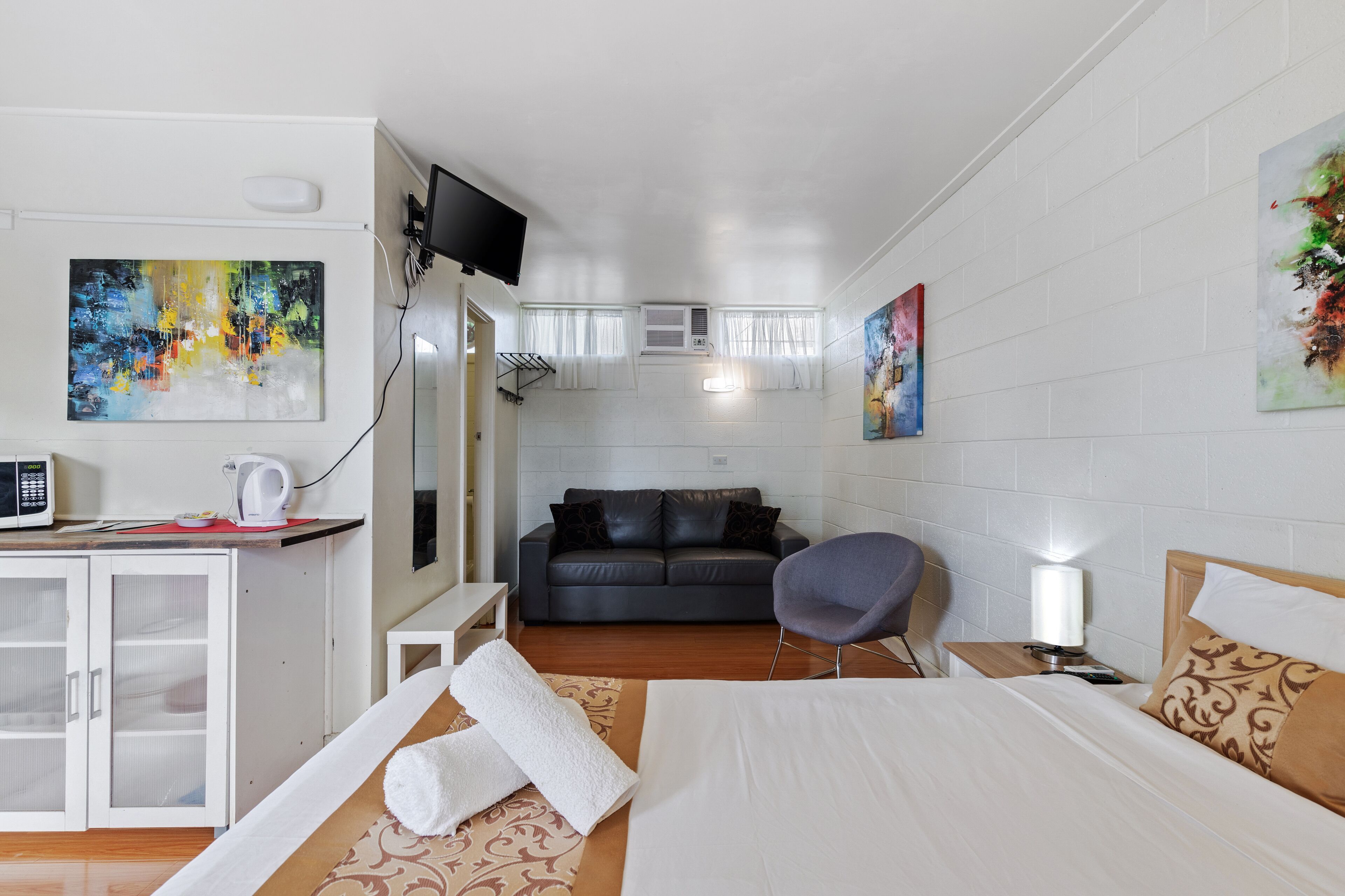Een hotelkamer met een bed, een bureau met een computer, een stoel, een televisie en kunstwerken aan de muren.