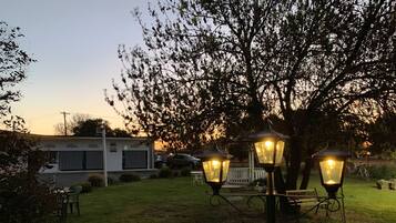 A backyard with a white building, a tree, and three lit lanterns.