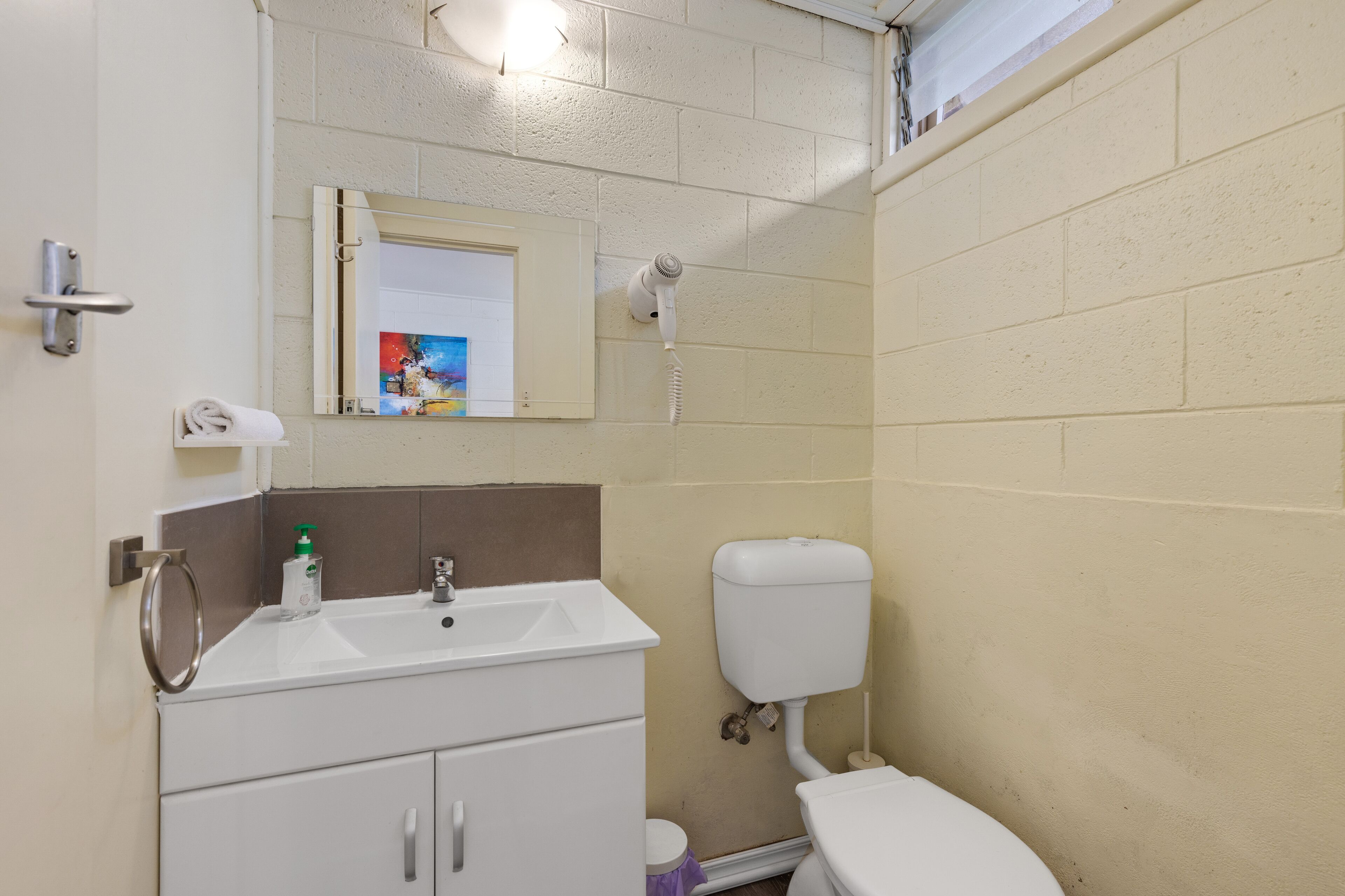 Ein Badezimmer mit Waschbecken, Spiegel, Toilette und einem an der Wand befestigten Föhn.