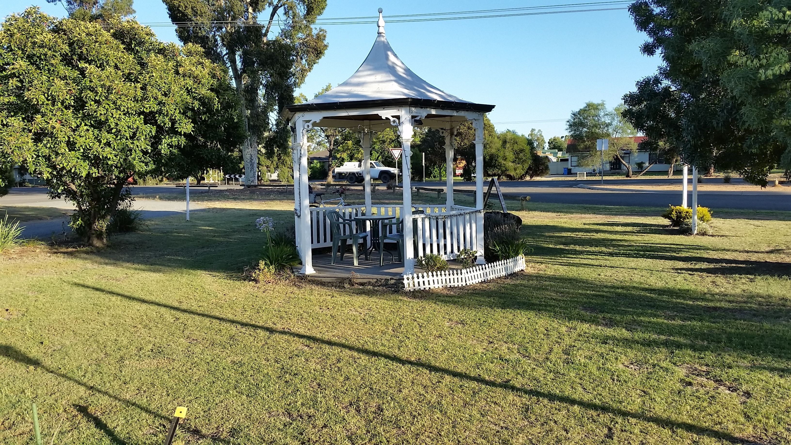A gazebo with a white roof and columns, surrounded by grass and trees.