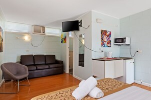 Quarto compacto com sofá, pequena escrivaninha, televisão e micro-ondas.