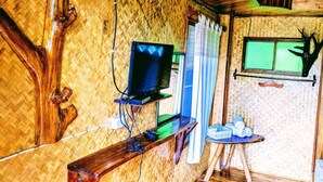A room with a television on a wooden stand, a small table with items, and a window with curtains. - Bansuanphuhong (Chiang Khan)
