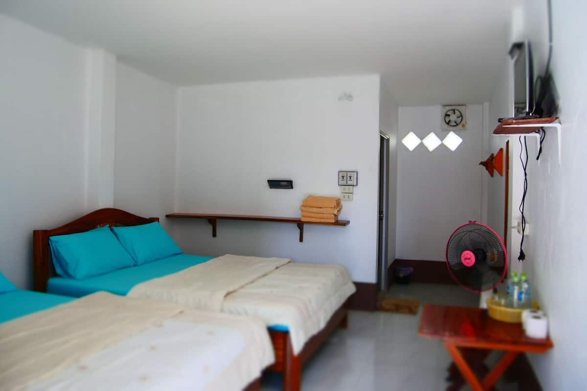 A room with two beds, a shelf with towels, a fan, and a clock on the wall.