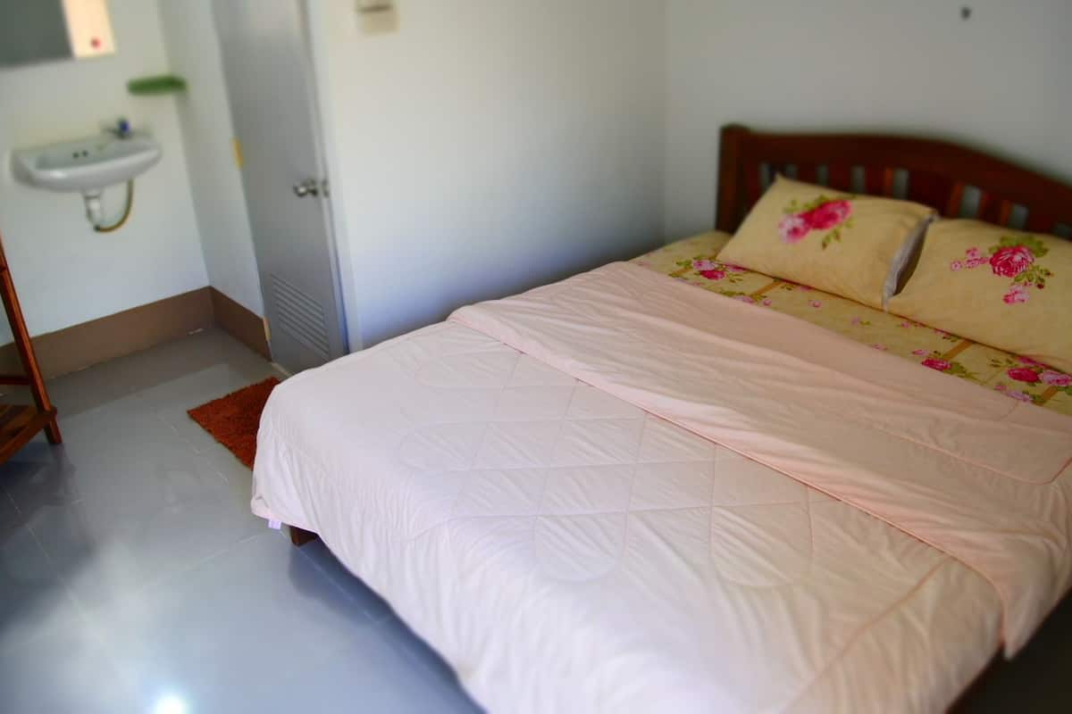 A bedroom with a bed, a wooden headboard, a bedside table, a red rug, and a white wall-mounted sink.