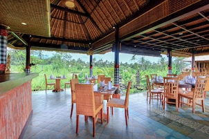 Un restaurante al aire libre con mesas y sillas de madera, techo de paja y vistas a vegetación exuberante.