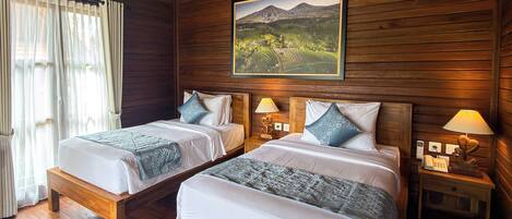 A room with two beds, wooden walls, a painting of a landscape, and bedside lamps.