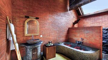 A bathroom with a stone sink, a wooden cabinet, a bathtub with red flowers, and a stone wall.