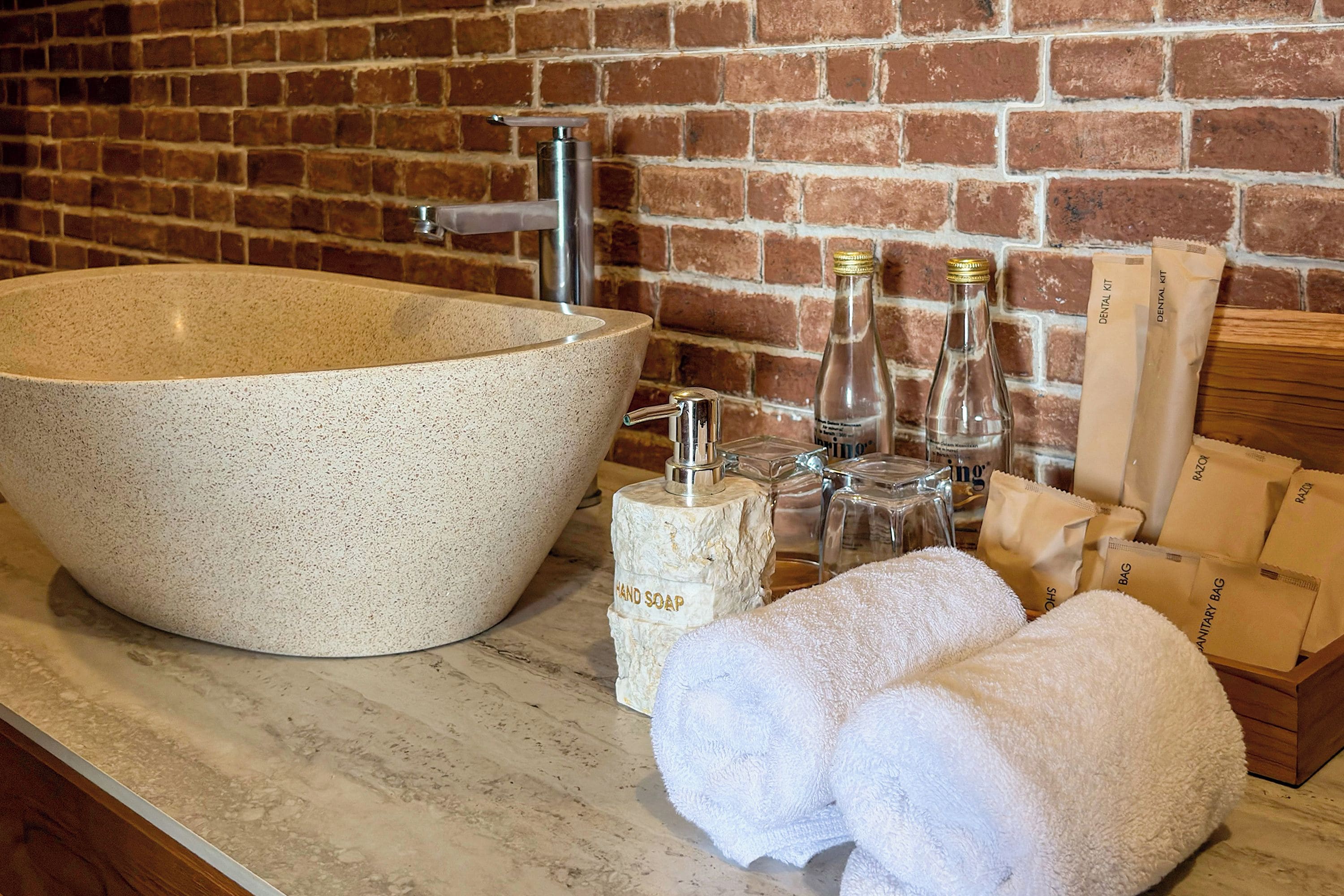 Un baño con un lavamanos grande color beige, un grifo, una botella de jabón para manos, una botella de enjuague bucal y una caja de madera con la etiqueta 'DENTAL KIT'.