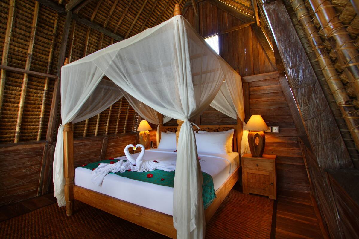 A four-poster bed with a canopy, bedside lamps, and a heart-shaped decoration on the bed.