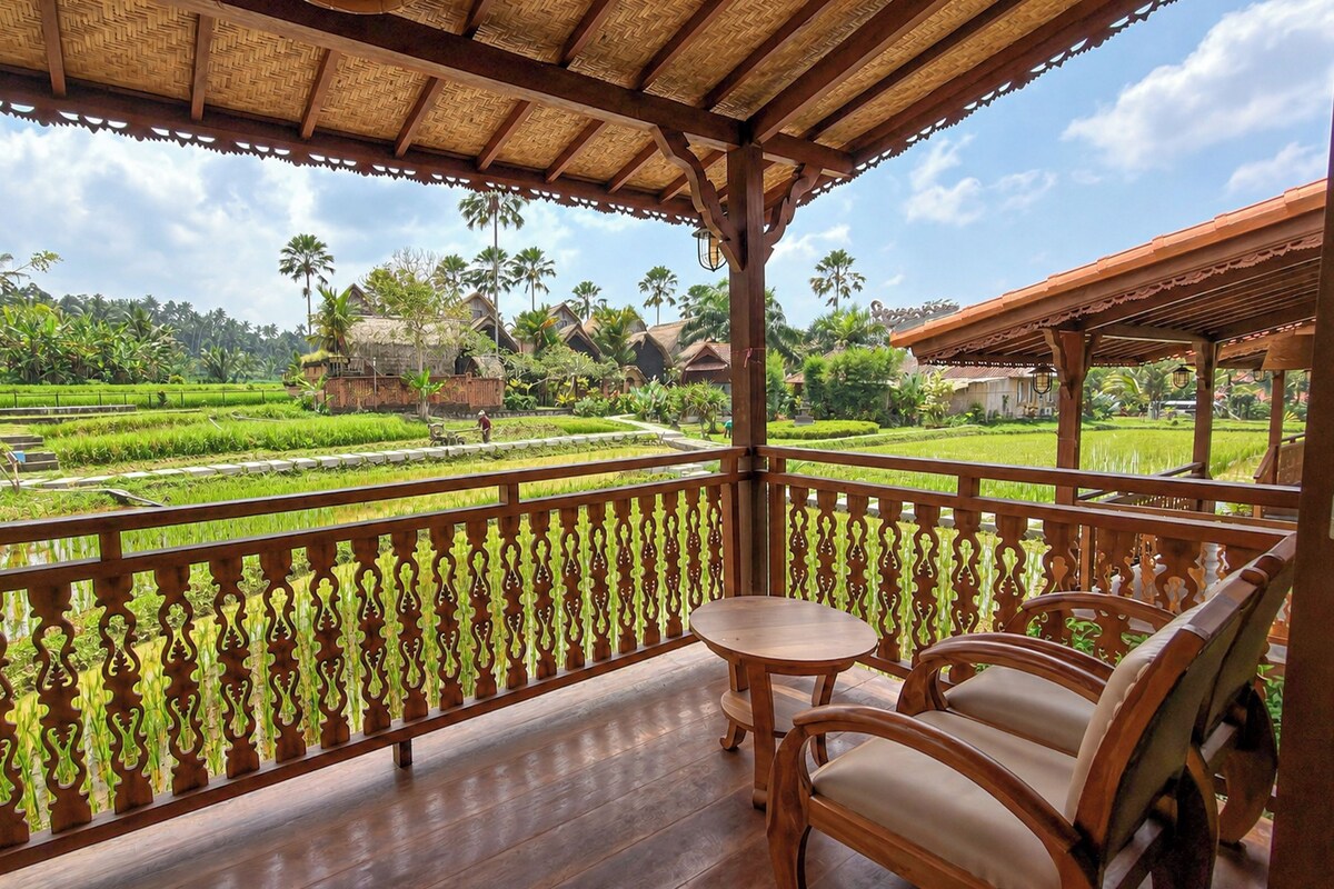 Un balcón de madera con vistas a un paisaje verde exuberante, que incluye campos de arroz y casas tradicionales.