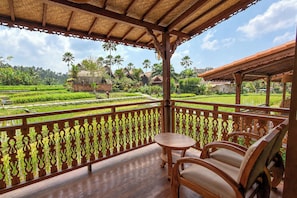 Een houten balkon met uitzicht op een weelderig groen landschap, met rijstvelden en traditionele huizen.