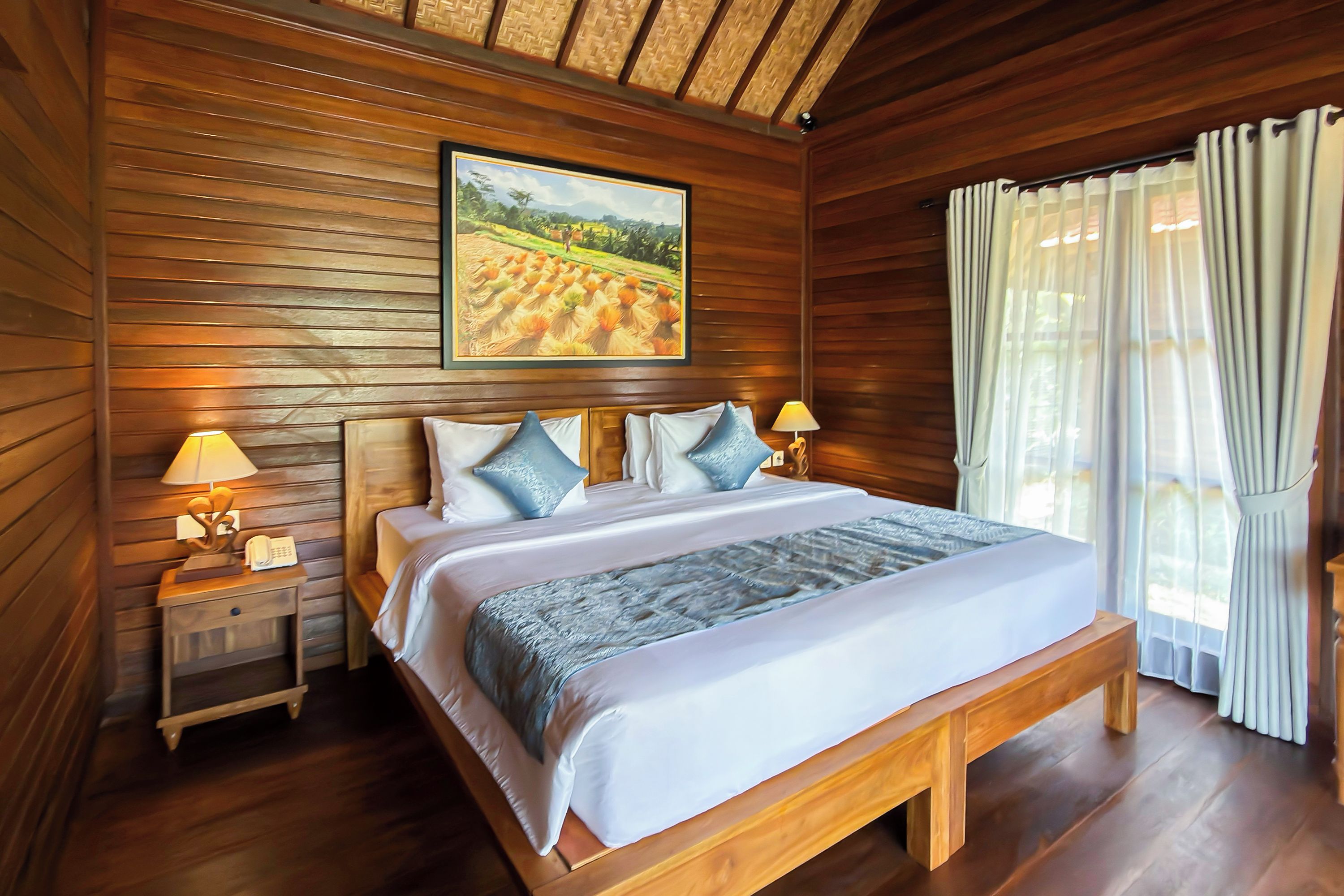 A wooden-paneled room with a large bed, two bedside tables with lamps, a painting on the wall, and a window with curtains.