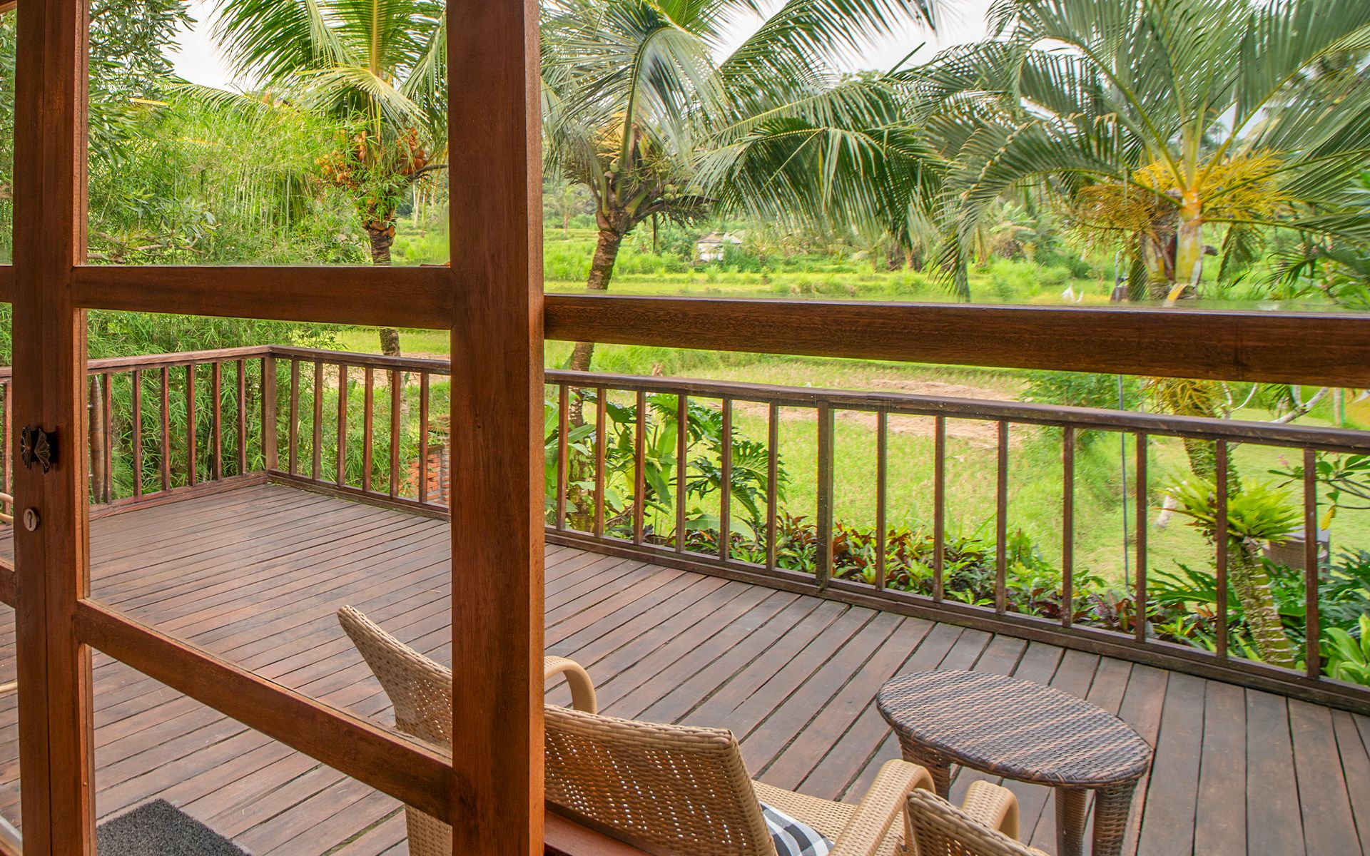 A wooden deck with wicker furniture, overlooking a lush garden with palm trees.