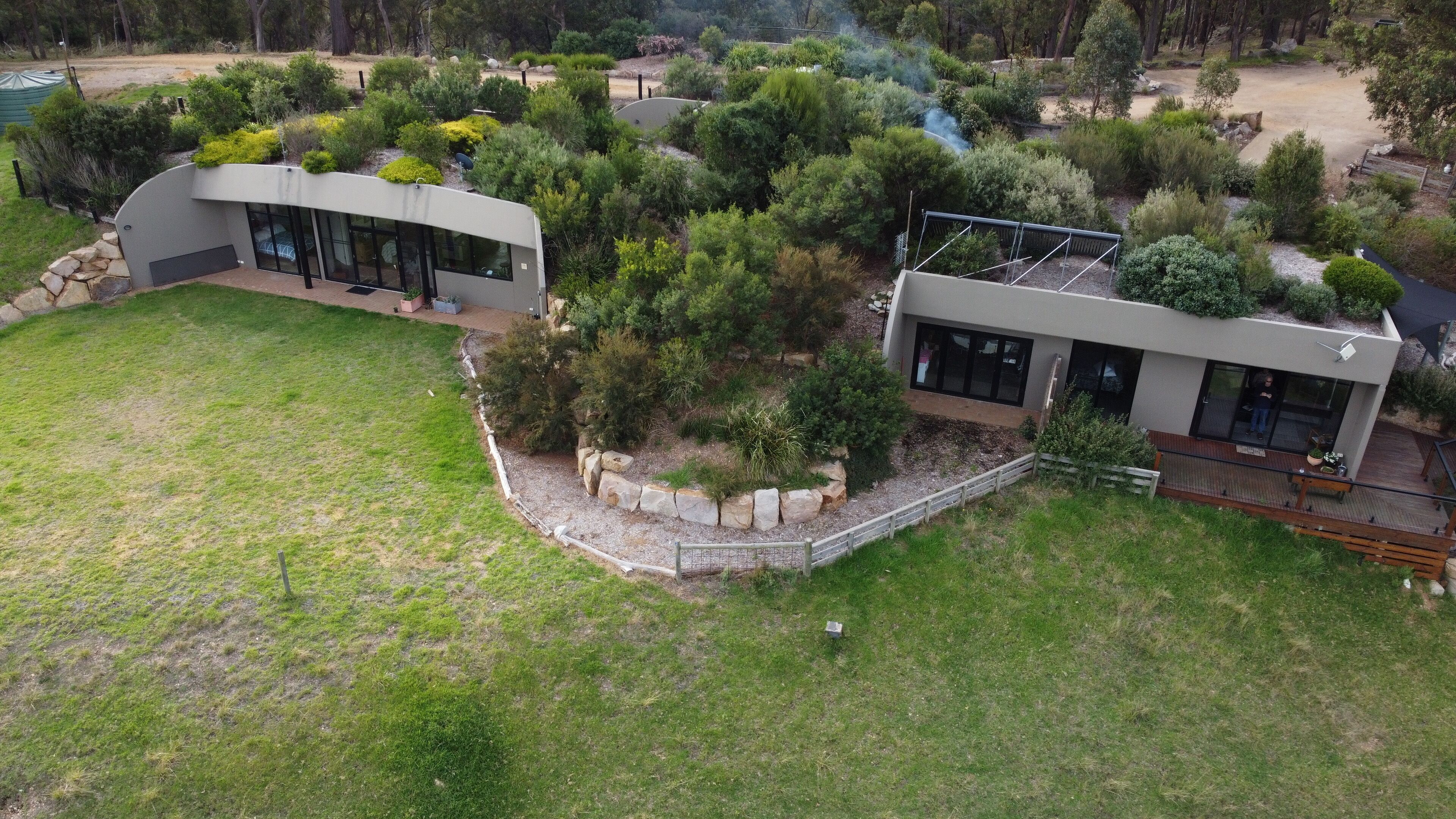 A modern house with two large glass windows, surrounded by a well-maintained garden with various shrubs and a stone border.