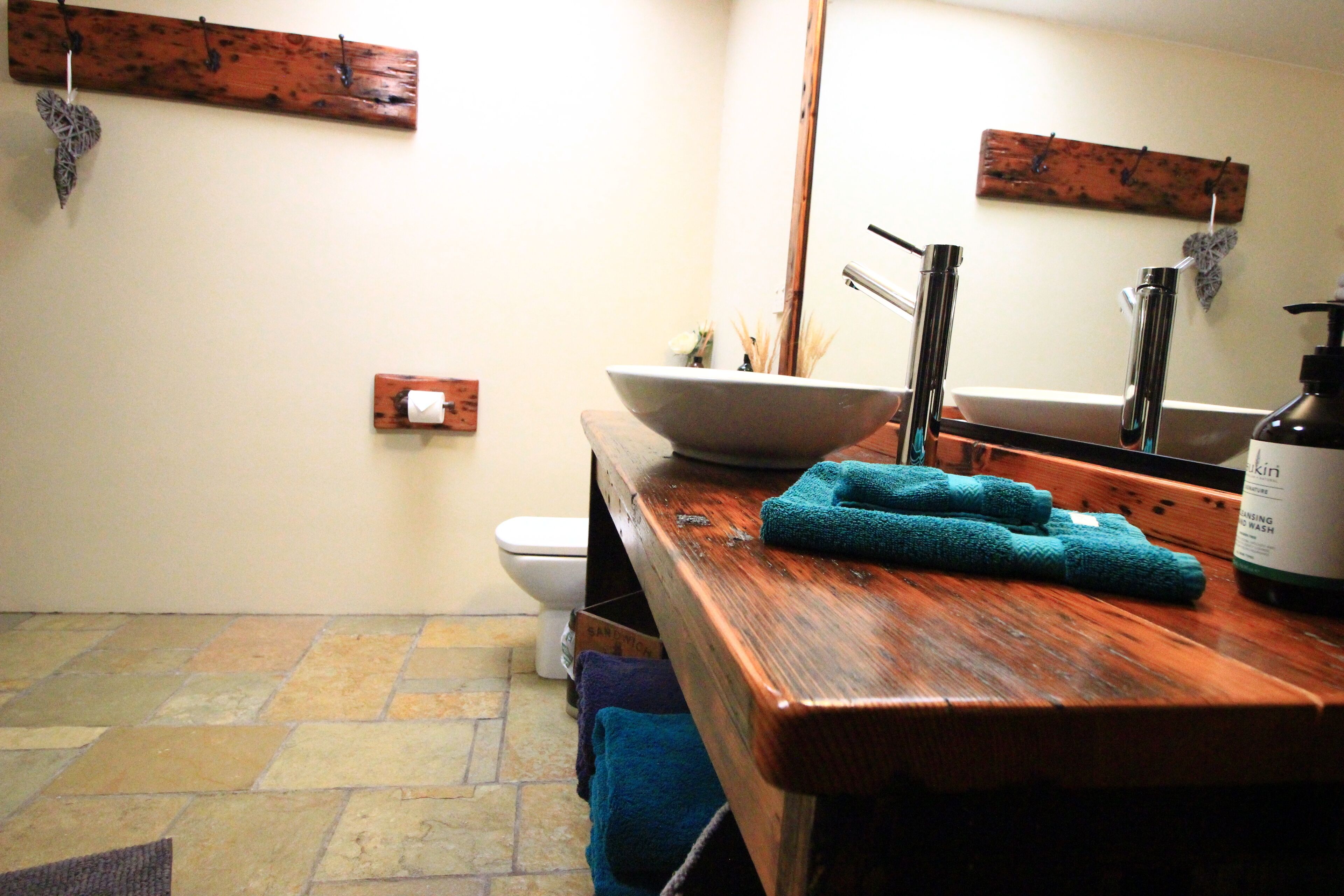 A bathroom with a wooden vanity, a large bowl sink, a toilet, and a mirror.