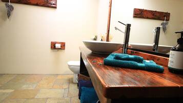 A bathroom with a wooden vanity, a large bowl sink, a toilet, and a mirror.