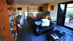 A living room with a black leather sofa, a coffee table, and a bookshelf. - Down to Earth Farm Retreat (Sarsfield)