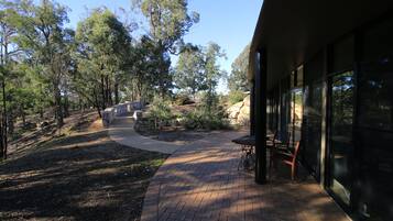 A paved pathway leading to a building with large windows, surrounded by trees and a stone wall.