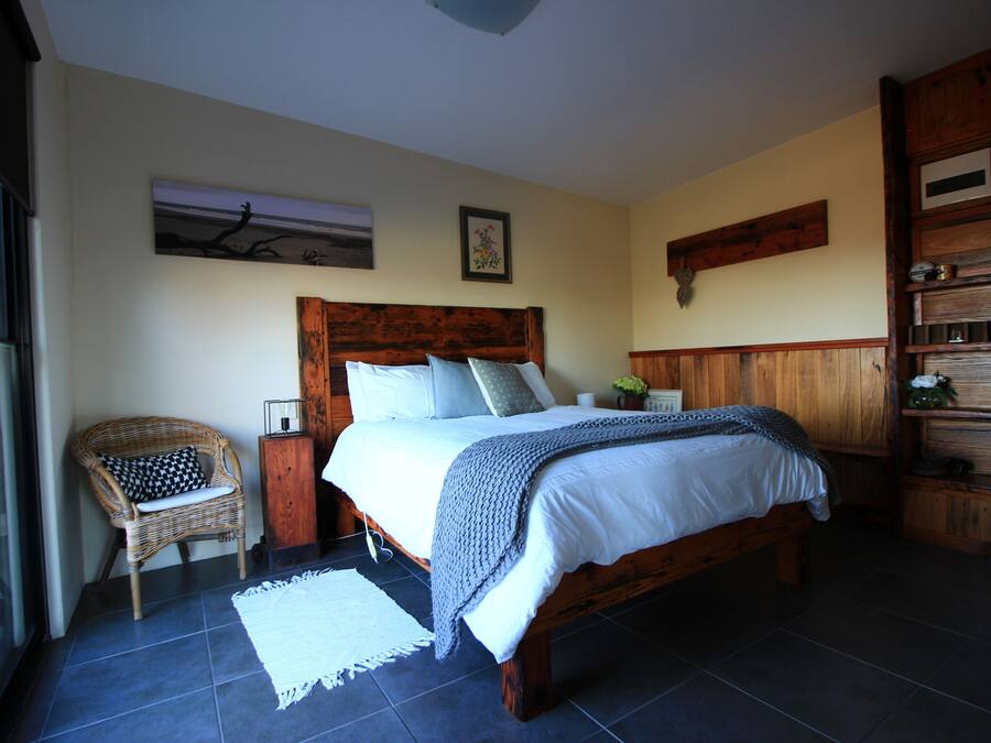 Een slaapkamer met een houten bed, een rieten stoel, een witte vloerkleed en een houten kast.