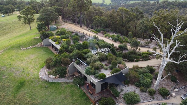 A modern house with a large deck, surrounded by dense greenery and a dirt road. - Down to Earth Farm Retreat (Sarsfield)