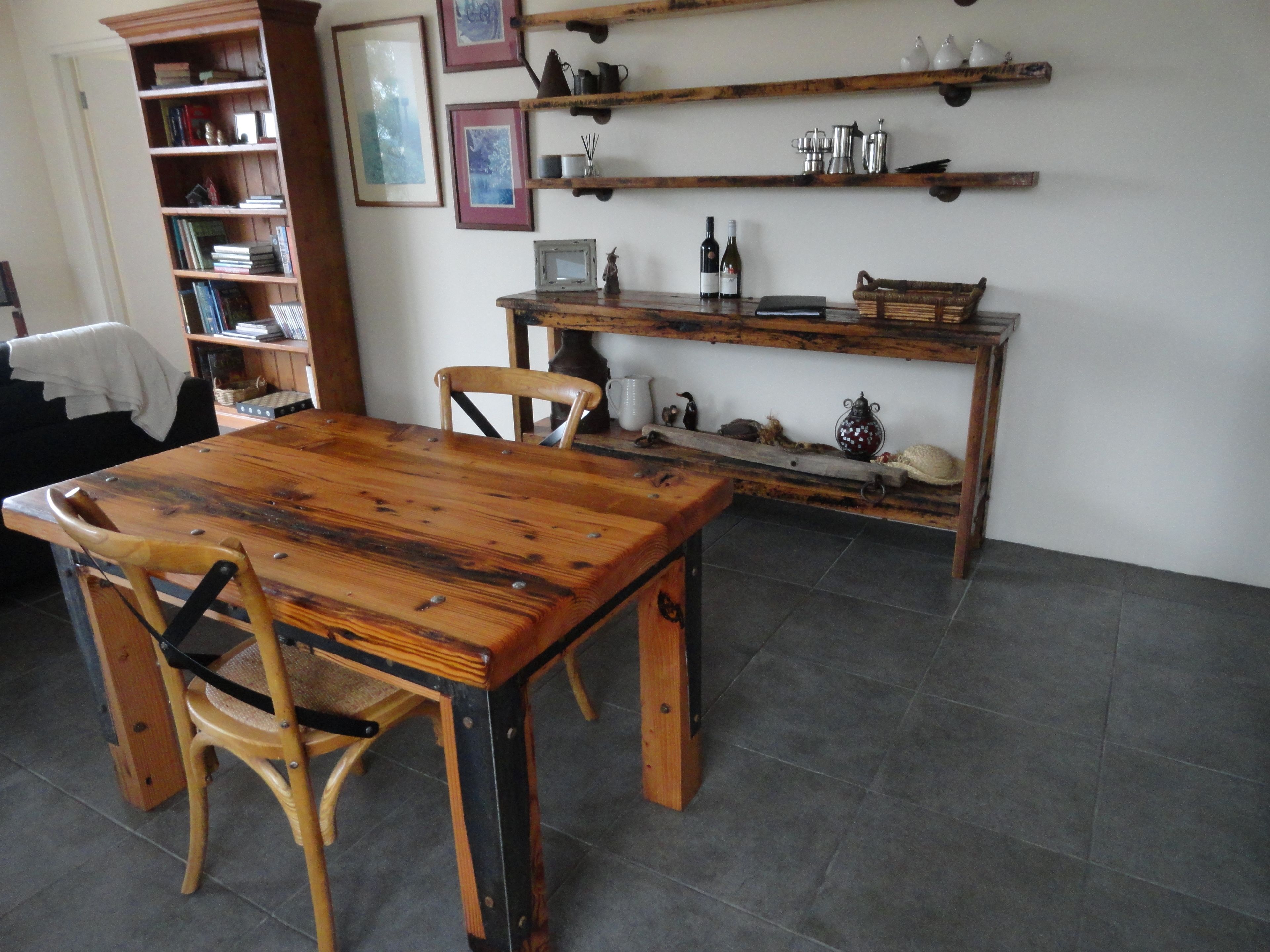 A dining area with a wooden table and chairs, a bookshelf, and shelves with kitchen items.