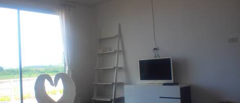 Un dormitorio con una cama grande, un televisor sobre un mueble blanco, una escalera y vistas al exterior.
