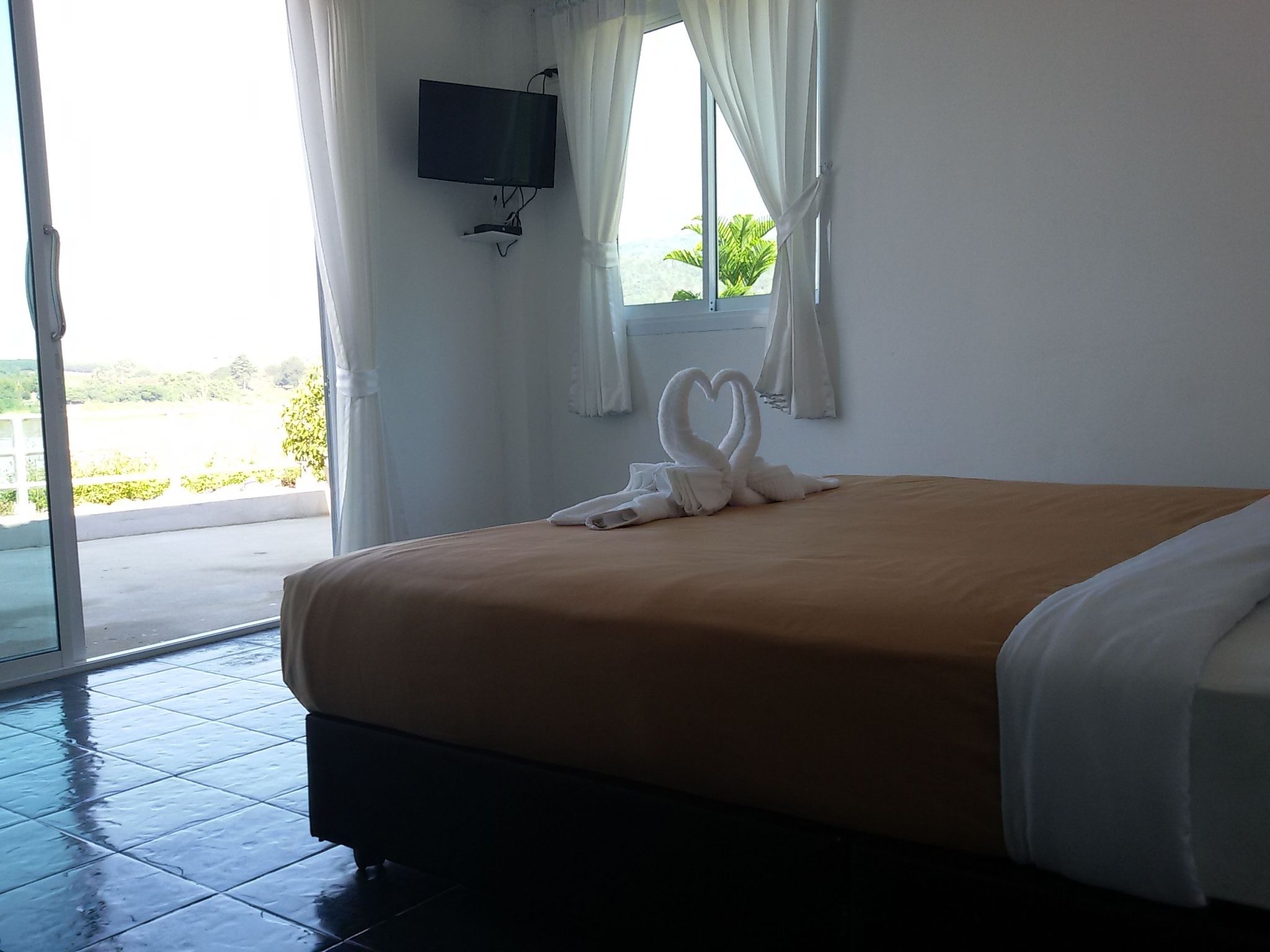 A hotel room with a bed, a TV mounted on the wall, and a view of the outdoors.