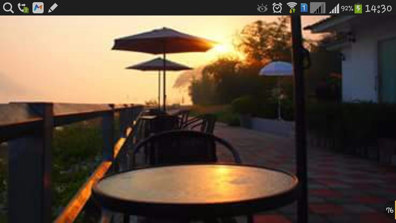 An outdoor seating area with tables and chairs, umbrellas, and a view of the sunset.