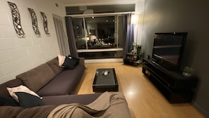 A living room with a sofa, a coffee table, a TV, and a sliding glass door leading to a dining area. - Apartment on Tennyson (Port Lincoln)