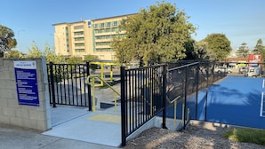 A gated parking area with a blue surface, a yellow handrail, and a signboard with text. - Apartment on Tennyson (Port Lincoln)