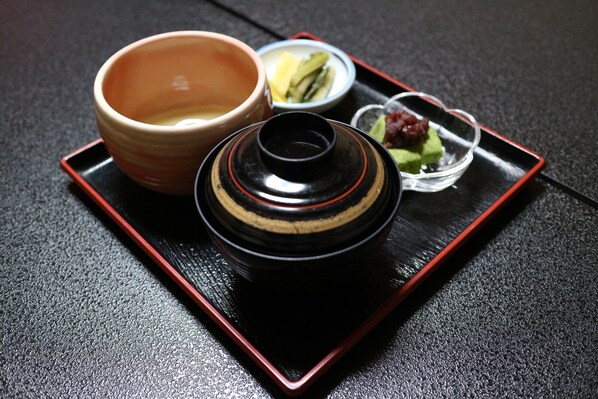 A tray with a ceramic bowl, a small dish with green food, and a black container with a lid.