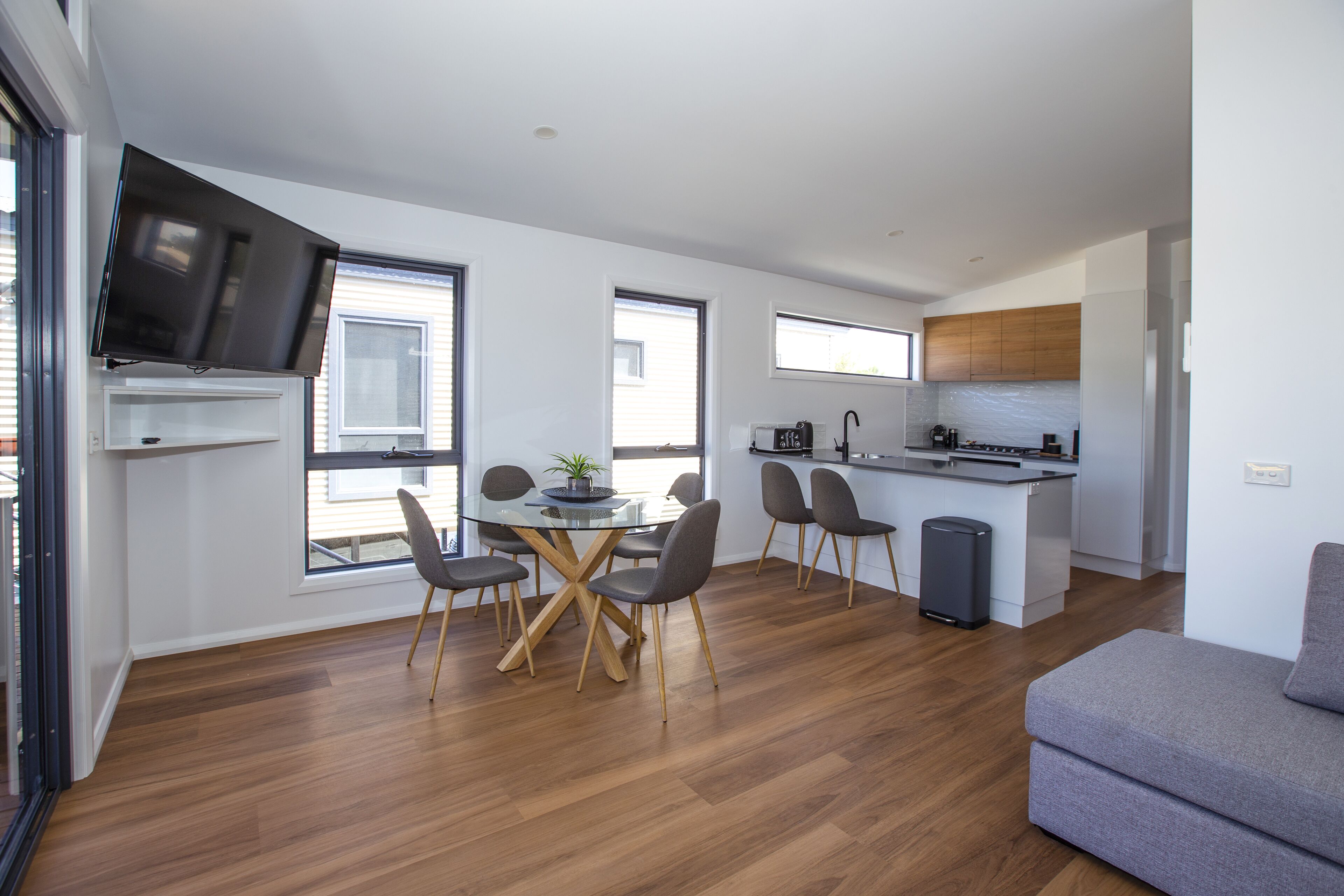 A modern kitchen with a central island, a dining area with a glass table and chairs, and a grey sofa.