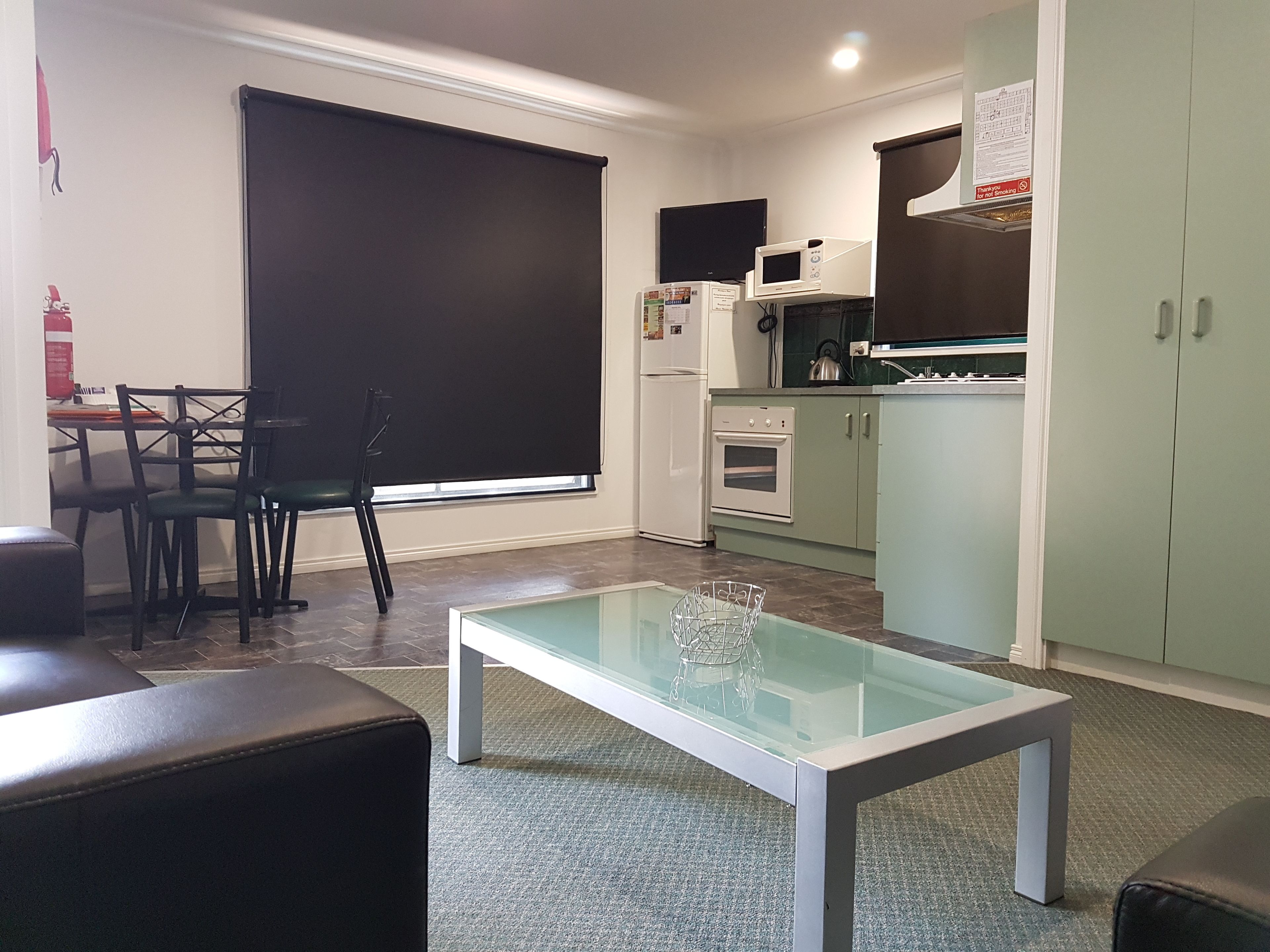 Een compacte keuken met een eethoek, een tafel met glazen blad en een zwarte stoel.