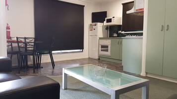 Een compacte keuken met een eethoek, een tafel met glazen blad en een zwarte stoel.