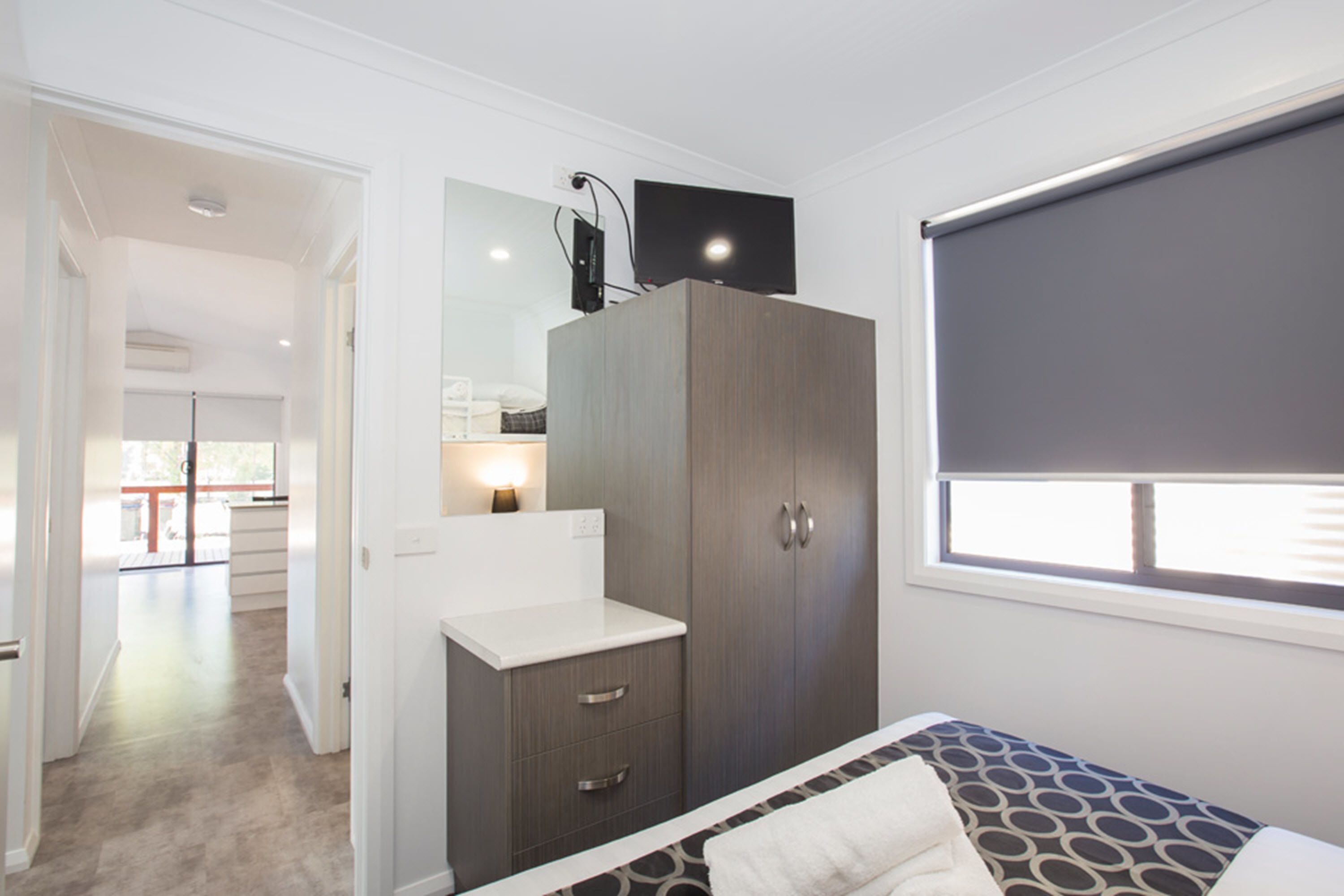 A bedroom with a bed, a wardrobe, a bedside table, a window with blinds, and a view of a balcony.