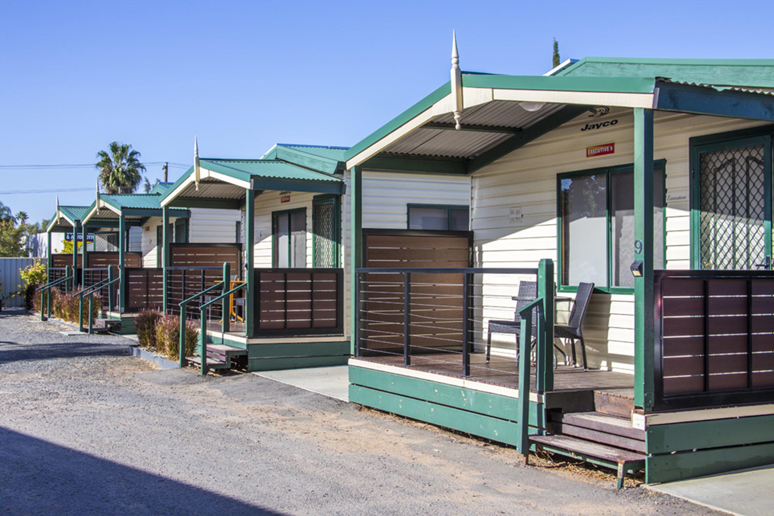 A row of mobile homes with green roofs and white walls, each with a small porch and steps leading to the entrance.