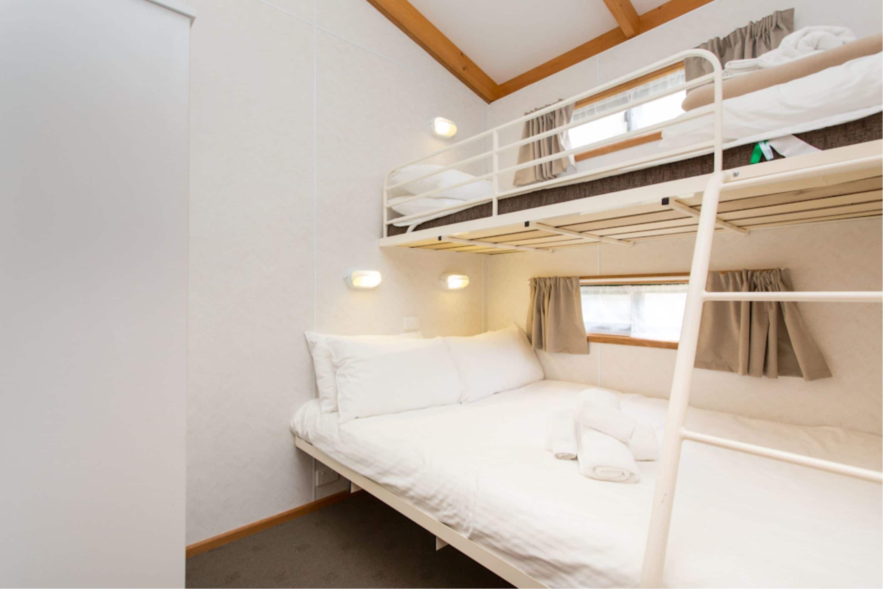 Quarto com beliche e uma cama de solteiro, ambos com roupa de cama branca.