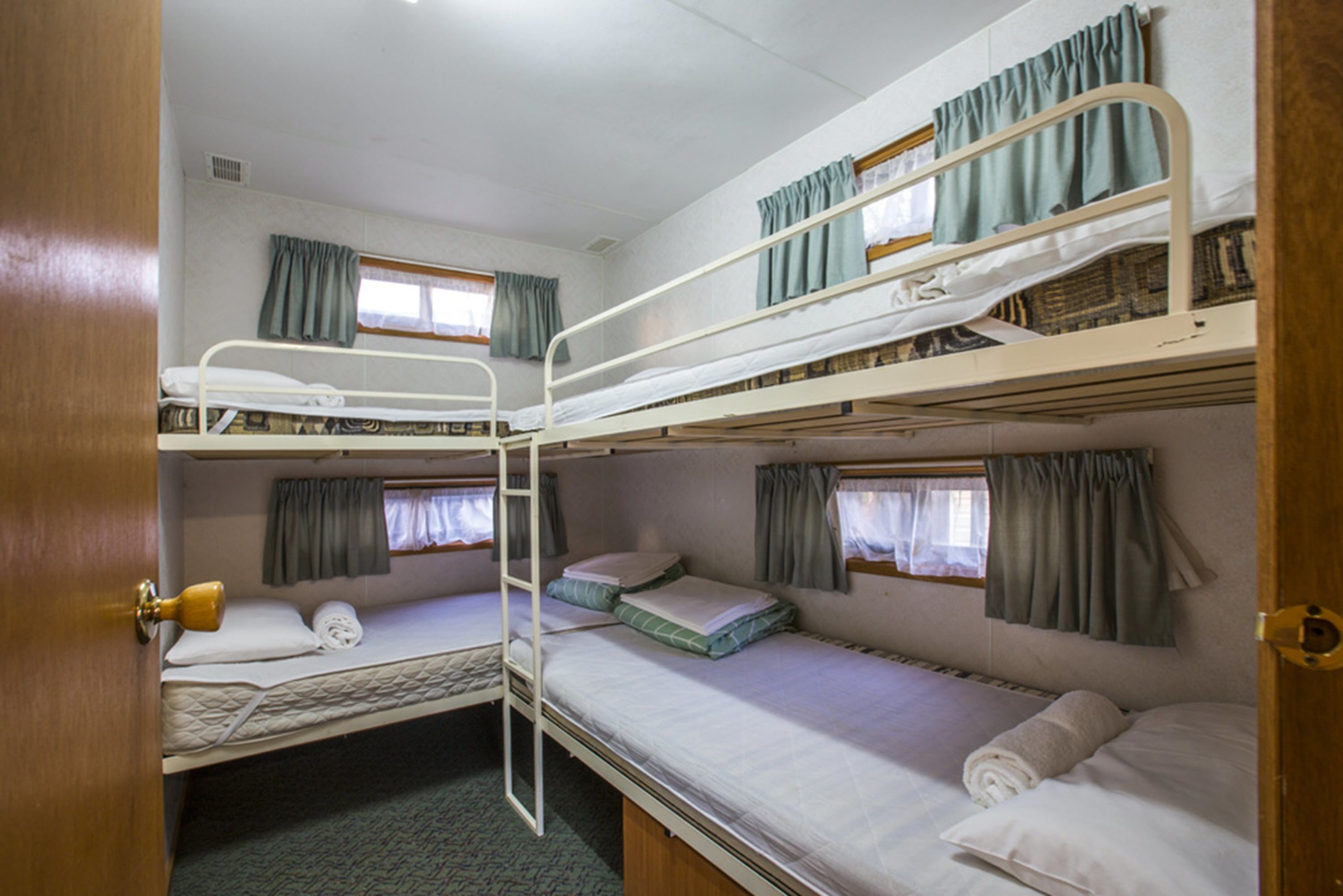A bunk bed room with three levels, each with a window and curtains. There is a door on the left side.