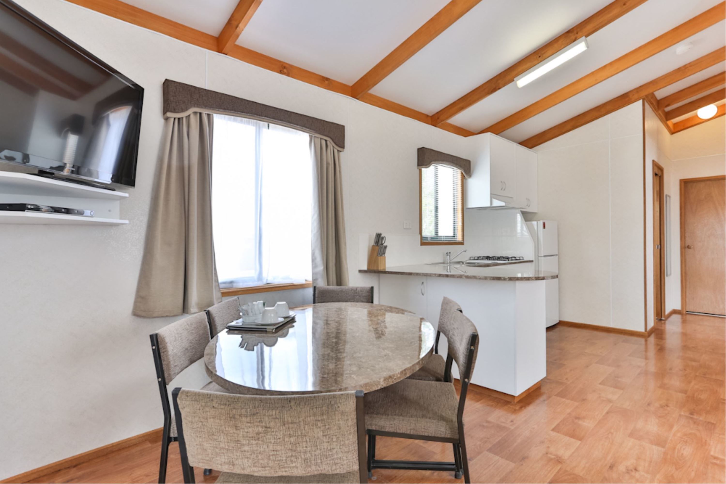 A modern kitchen with a central island, a dining area with a round table and chairs, and a large window with curtains.