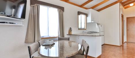 A modern kitchen with a central island, a dining area with a round table and chairs, and a large window with curtains.