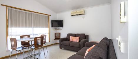 Una sala de estar con sofá, televisor y comedor con sillas y mesa.