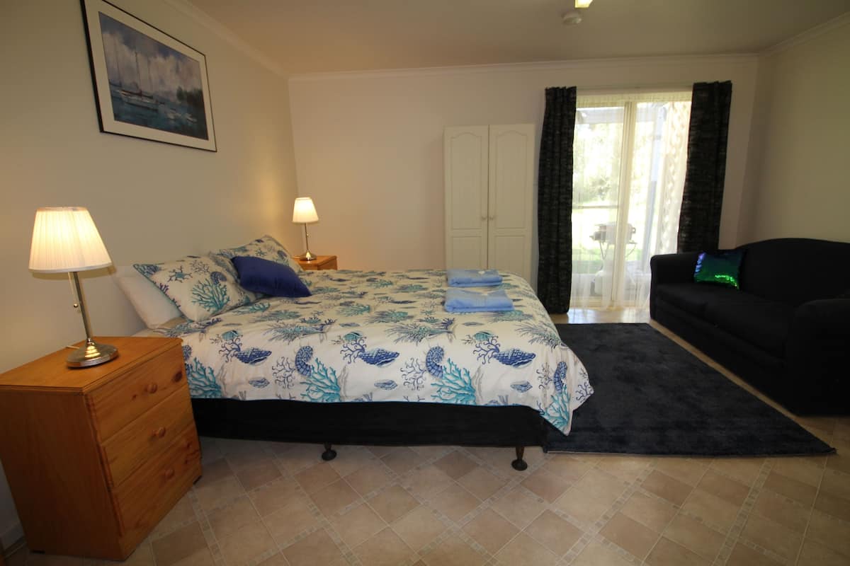 Un dormitorio con cama, cómoda, mesita de noche, sofá negro y puerta que da a un balcón.