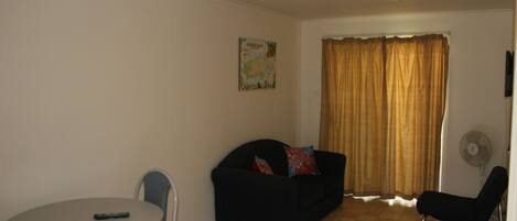A small living area with a round table, a sofa, and a single chair. A map is hung on the wall, and a window with curtains is visible.