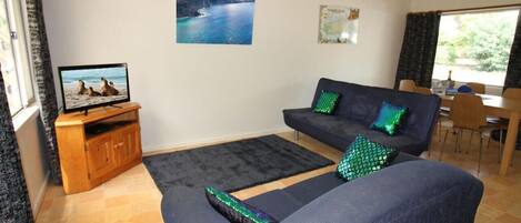 A living room with a sofa, a television on a wooden stand, a rug, and a window with curtains.