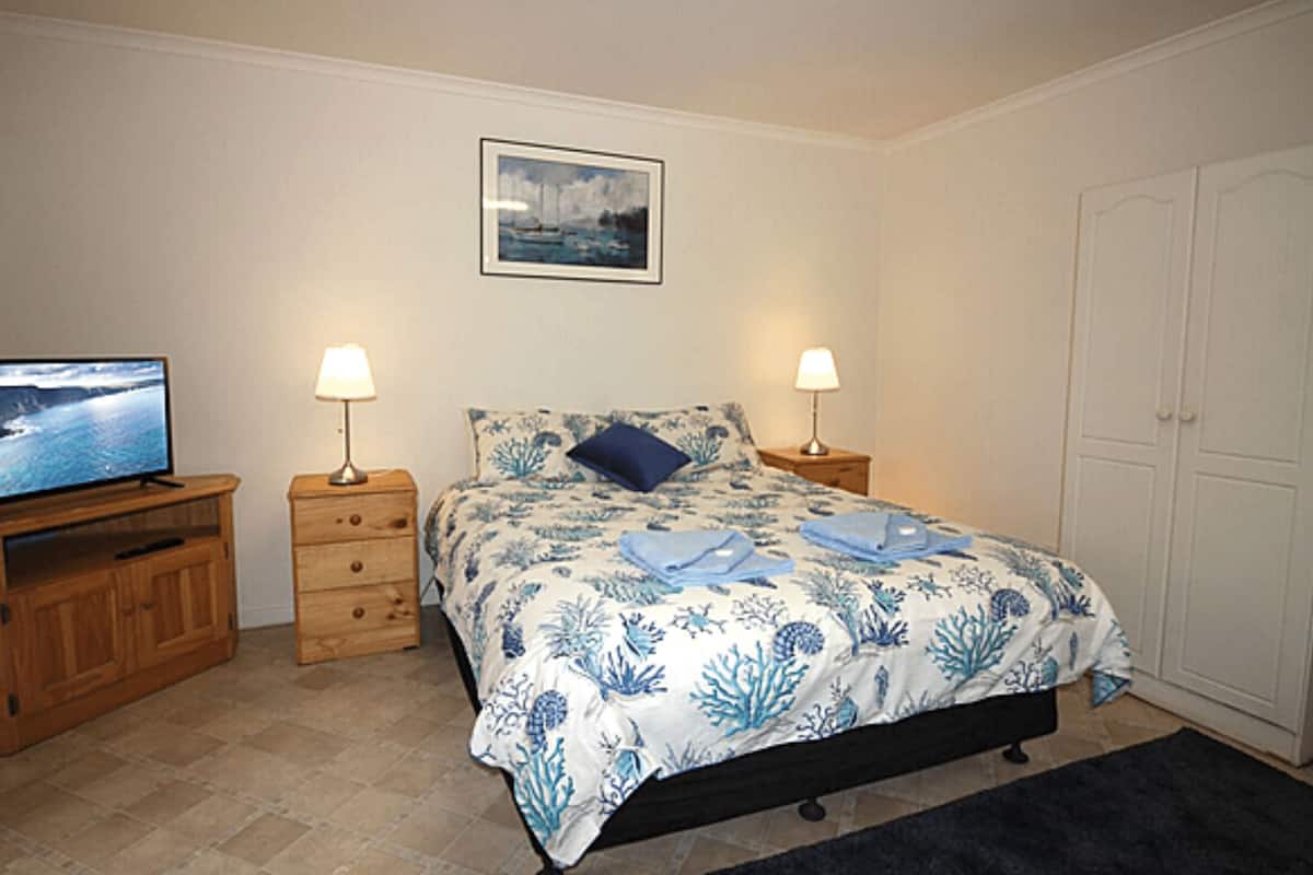 Un dormitorio con cama, dos mesitas de noche con lámparas, un televisor sobre un mueble de madera y un armario.
