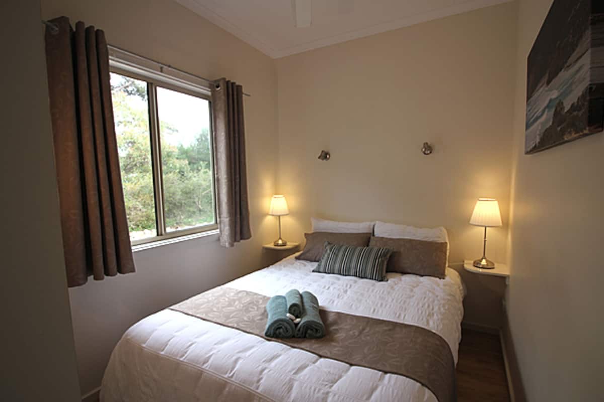 Un dormitorio con una cama grande, dos lámparas de noche, una ventana con cortinas y un cuadro en la pared.