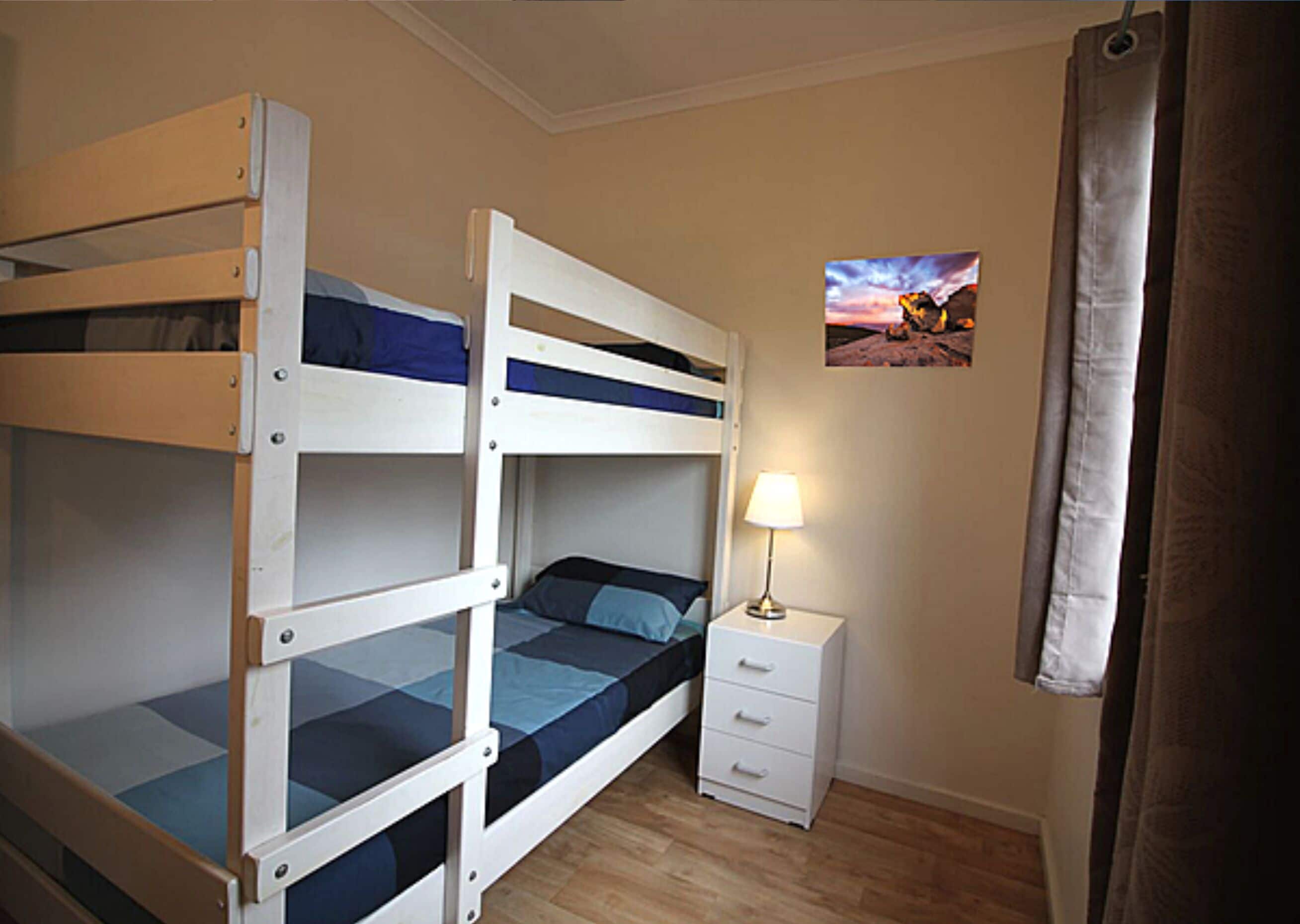 Une chambre avec un lit superposé, une table de chevet et une lampe.