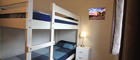 Une chambre avec un lit superposé, une table de chevet et une lampe.