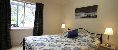 A bedroom with a bed, two bedside tables with lamps, a window with curtains, and a wall-mounted picture.